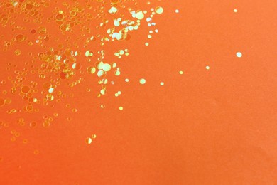 Photo of Shiny bright golden glitter on orange background. Space for text