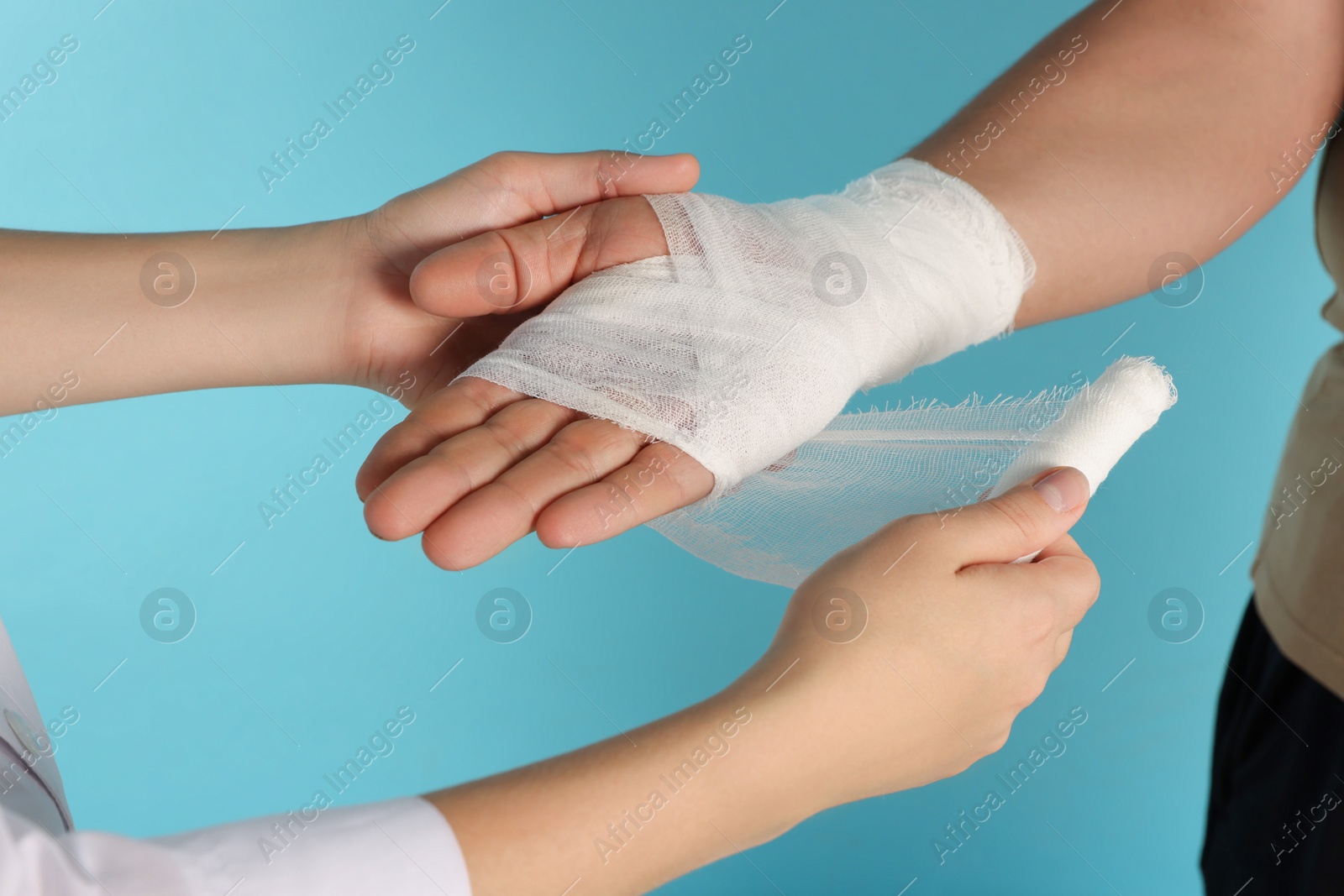 Photo of Doctor applying bandage onto patient's hand on light blue background, closeup