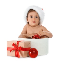 Cute little baby wearing Santa hat sitting in box with Christmas gift on white background