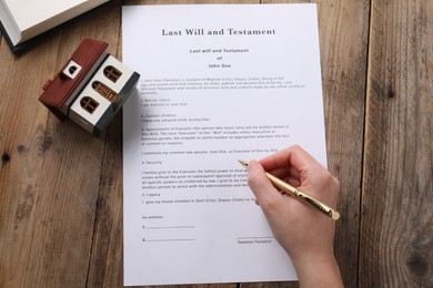 Photo of Woman signing Last Will and Testament at wooden table, top view