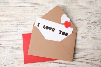 Photo of Card with phrase I Love You in envelope and paper hearts on white wooden table, flat lay