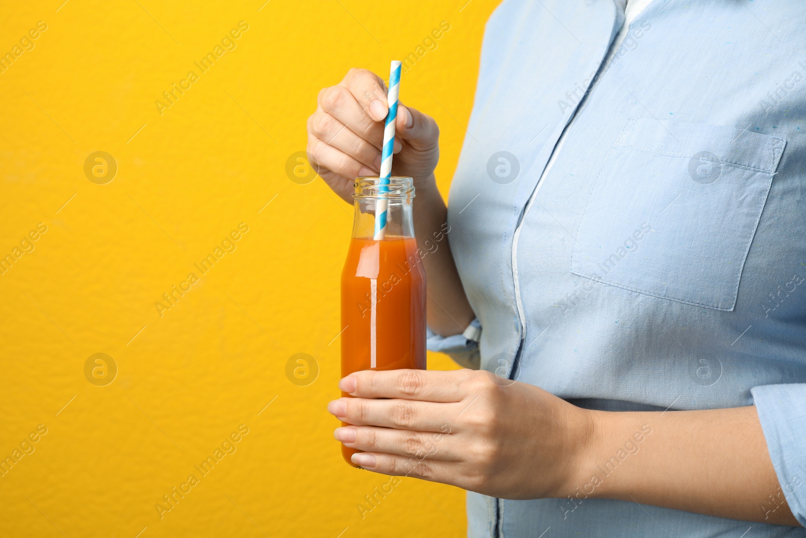 Photo of Woman holding bottle of tasty carrot juice on color background, closeup. Space for text