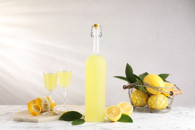 Photo of Tasty limoncello liqueur, lemons and green leaves on white marble table