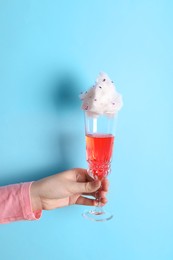 Woman holding glass of cotton candy cocktail on light blue background, closeup