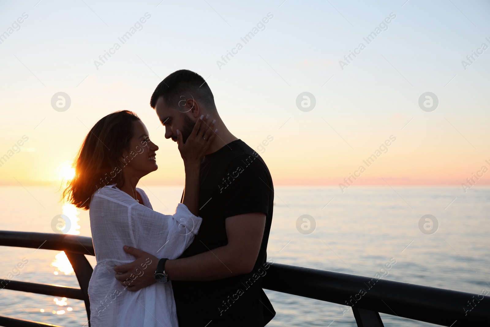 Photo of Happy young couple hugging on sea embankment at sunset