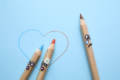 Photo of Pencils with drawn faces on light blue background, flat lay. Concept of jealousy