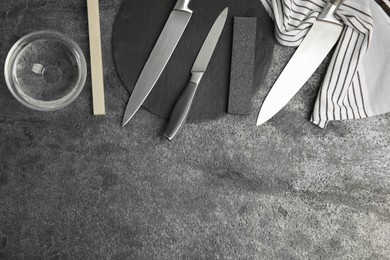 Photo of Sharpening stones, knives and water on grey table, flat lay. Space for text