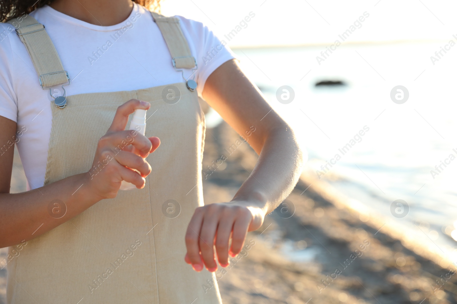 Photo of Young woman using insect repellent on beach, closeup