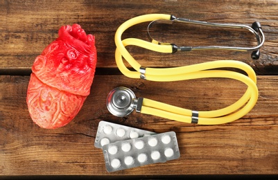 Photo of Stethoscope, pills and model of heart on wooden background. Heart attack concept