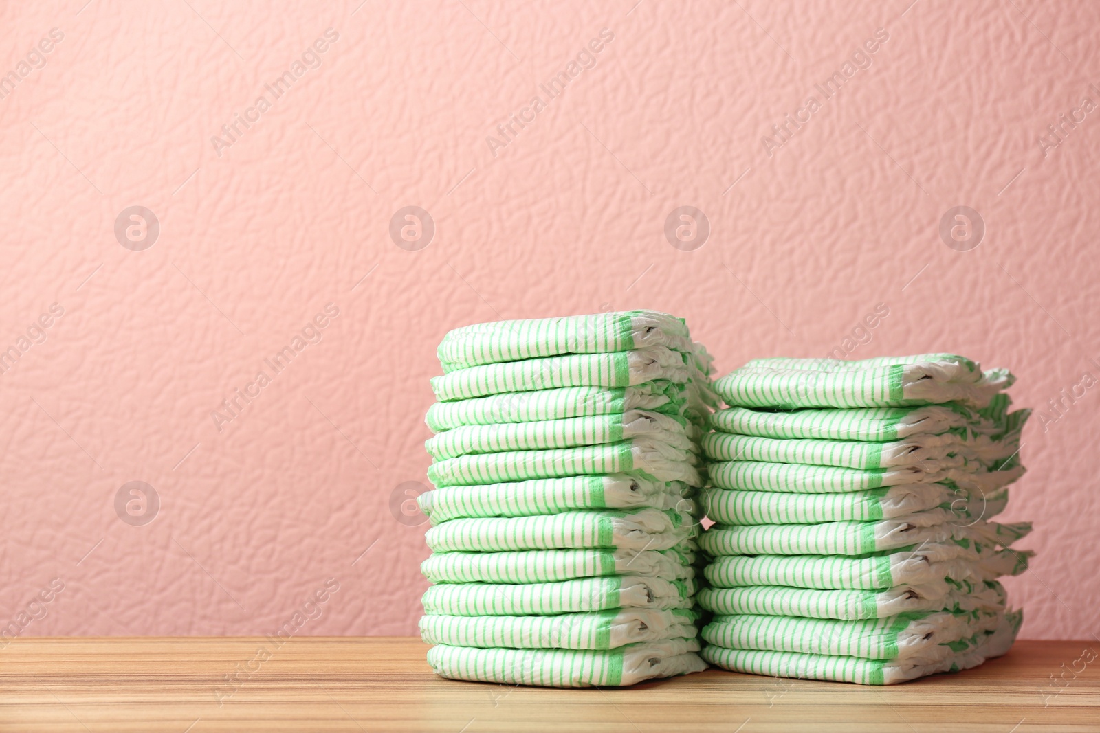 Photo of Stacks of diapers on table against color background, space for text. Baby accessories