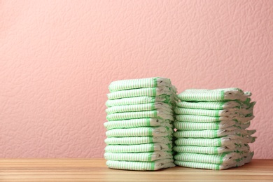 Stacks of diapers on table against color background, space for text. Baby accessories