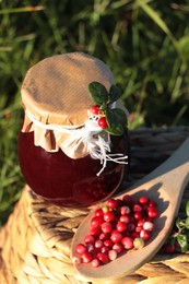 Jar of delicious lingonberry jam and red berries on wicker basket outdoors