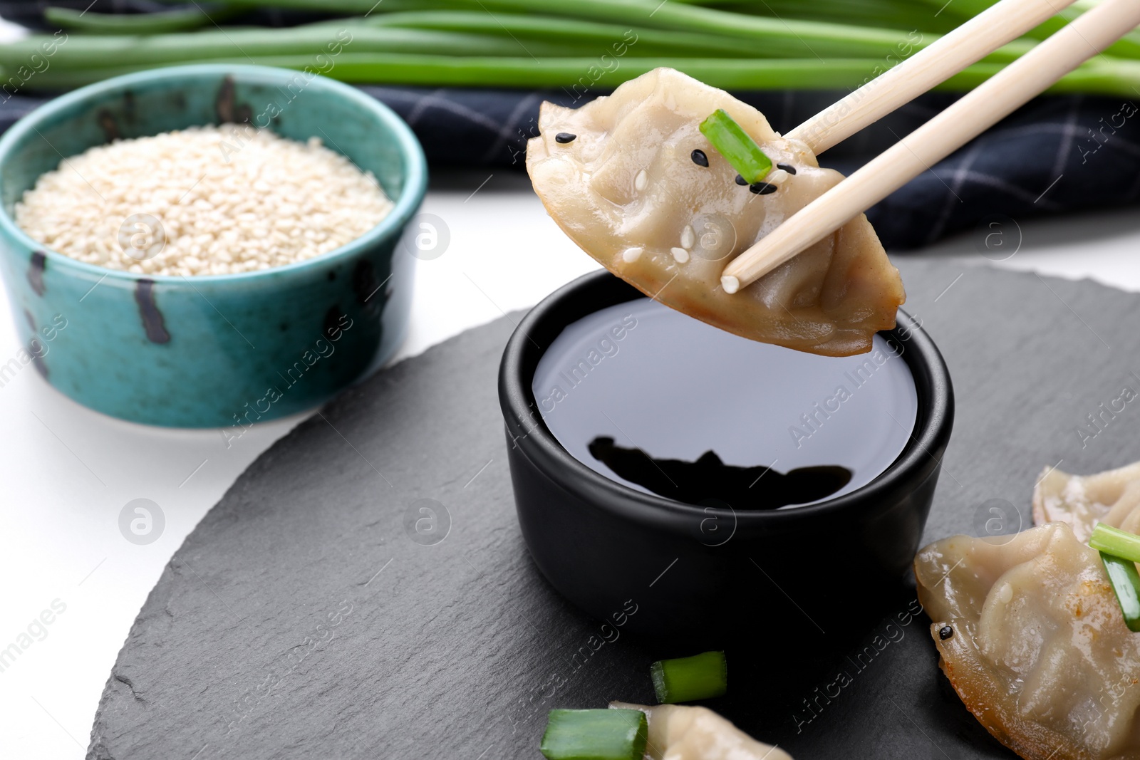Photo of Holding delicious gyoza (asian dumpling) with chopsticks above soy sauce on white table, closeup