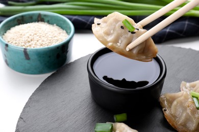 Holding delicious gyoza (asian dumpling) with chopsticks above soy sauce on white table, closeup