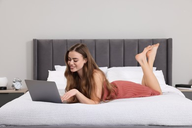 Happy woman with laptop on bed in bedroom