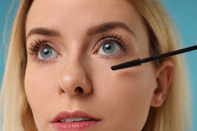 Photo of Beautiful woman applying mascara on light blue background, closeup