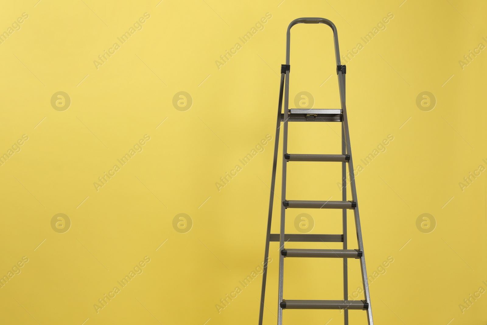 Photo of Metal stepladder on yellow background. Space for text