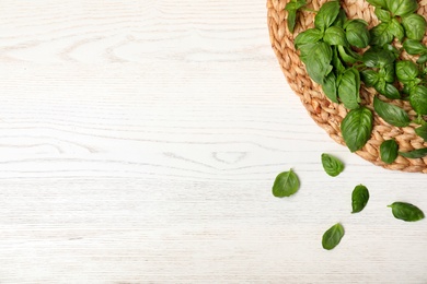 Photo of Wicker mat and fresh basil leaves on table, top view with space for text