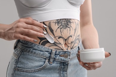 Photo of Woman applying healing cream onto her tattoos against grey background, closeup