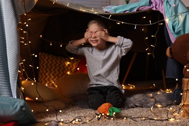 Photo of Happy boy covering his eyes in decorated play tent at home