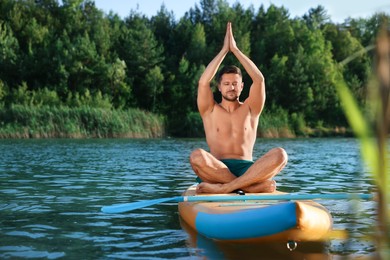 Photo of Man practicing yoga on color SUP board on river