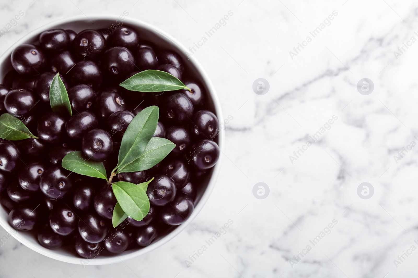 Photo of Fresh acai berries in bowl on white marble table, top view. Space for text