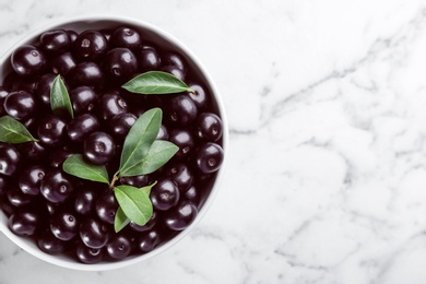 Fresh acai berries in bowl on white marble table, top view. Space for text