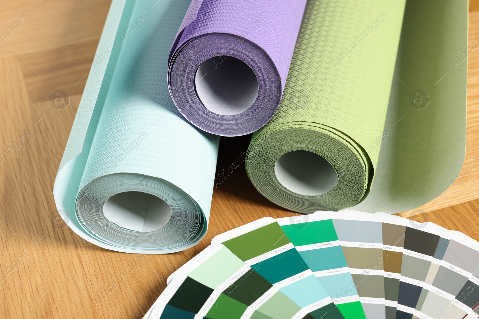 Photo of Different wallpaper rolls and color palette samples on wooden table