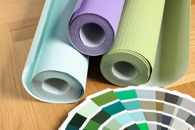 Photo of Different wallpaper rolls and color palette samples on wooden table