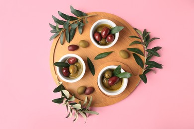 Wooden tray with different ripe olives and leaves on pink background, flat lay