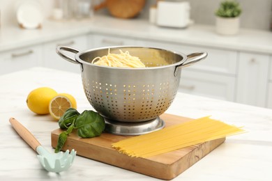 Photo of Cooked pasta in metal colander and products on white marble table, closeup