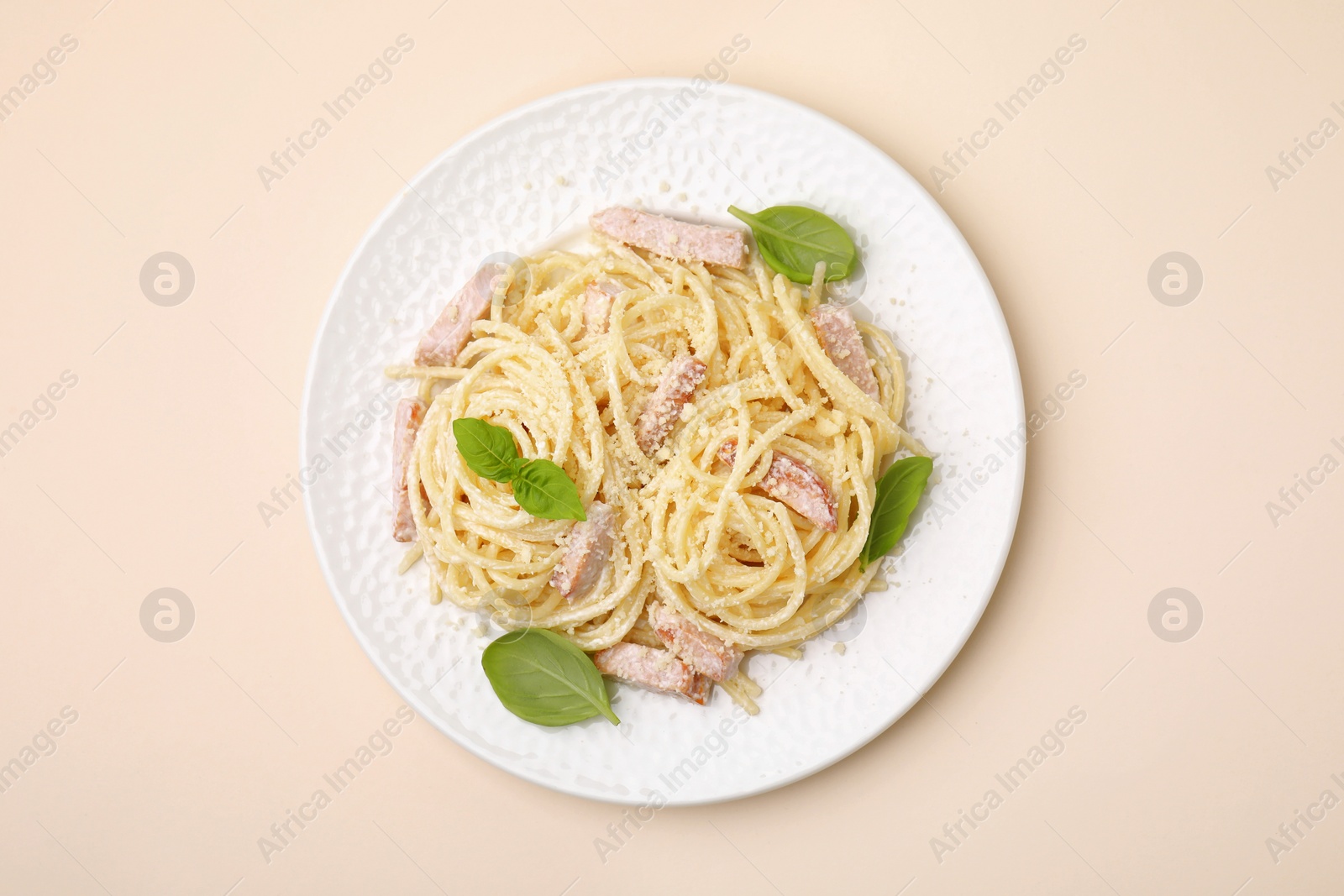 Photo of Plate of tasty pasta Carbonara with basil leaves on beige background, top view