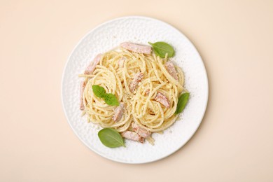 Plate of tasty pasta Carbonara with basil leaves on beige background, top view