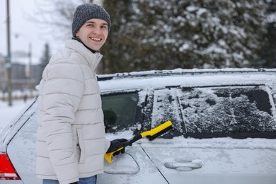 Man cleaning snow from car with brush outdoors