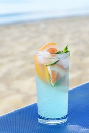 Glass of refreshing drink with grapefruit and mint on blue lounger at beach