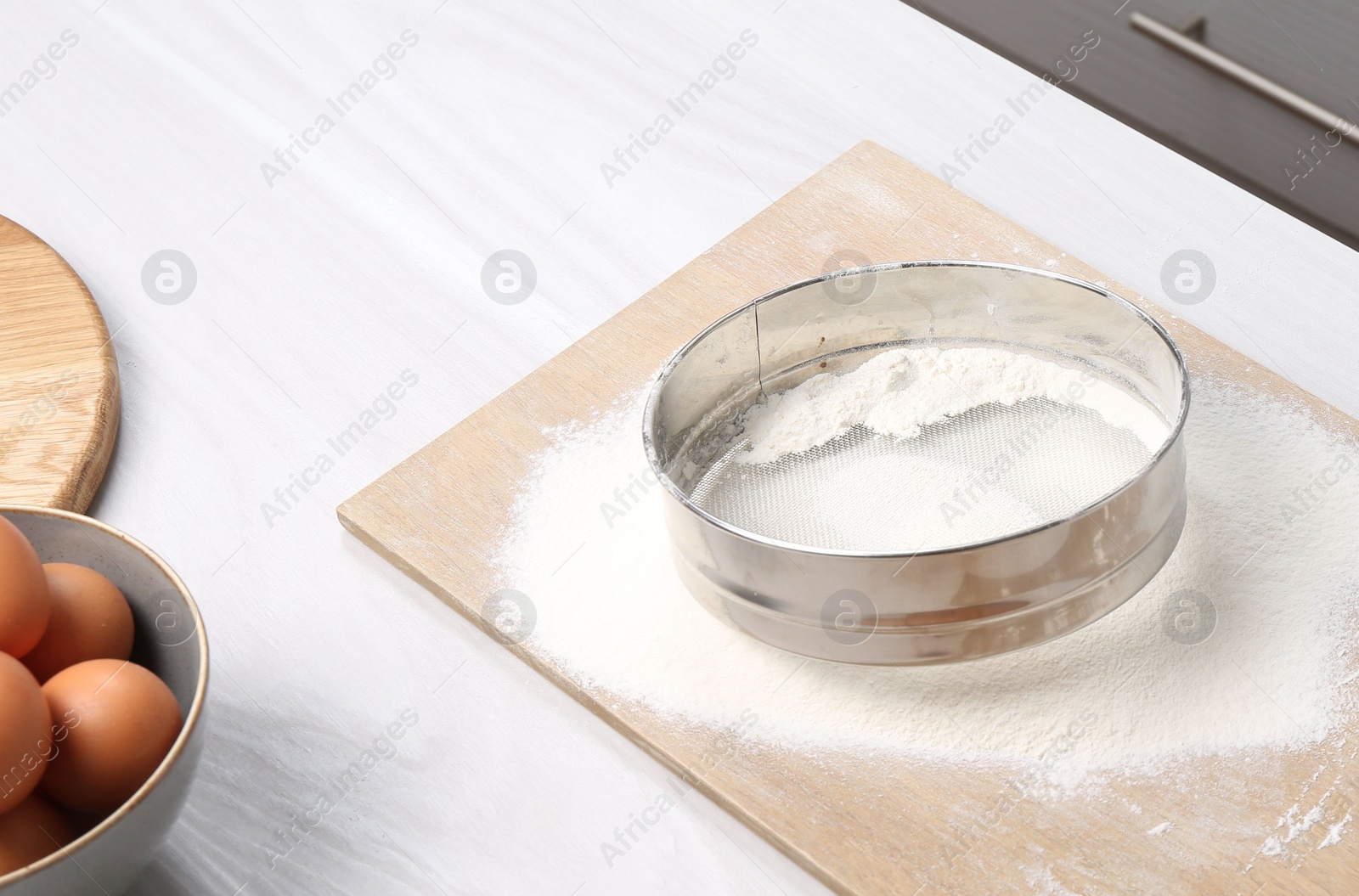 Photo of Sieve with flour, eggs and rolling pin on table in kitchen