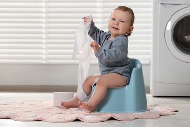 Photo of Little child with toilet paper roll sitting on plastic baby potty indoors. Space for text