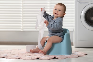 Little child with toilet paper roll sitting on plastic baby potty indoors. Space for text