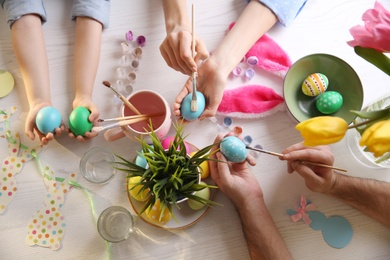Photo of Father, mother and their child painting Easter eggs at white table, top view