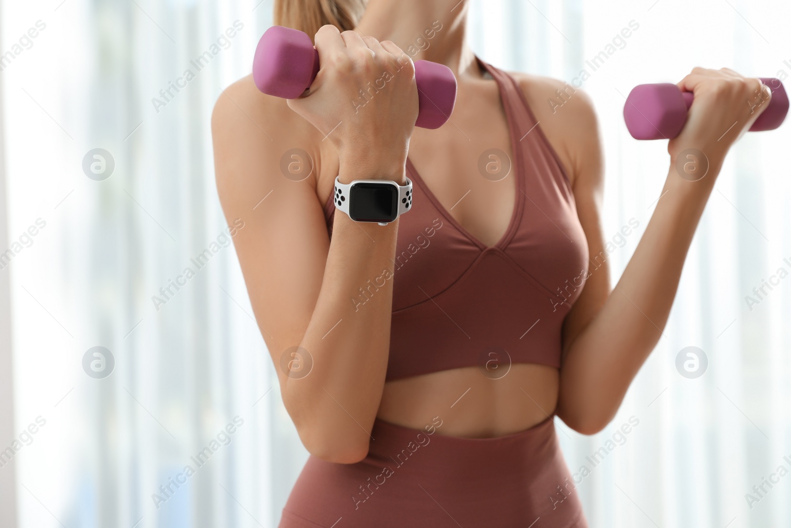 Photo of Young woman wearing smart watch during training indoors, closeup