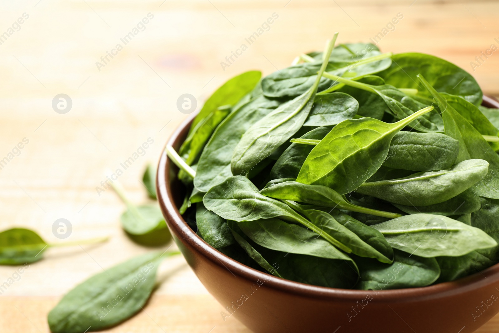 Photo of Bowl of fresh green healthy spinach on wooden table, closeup