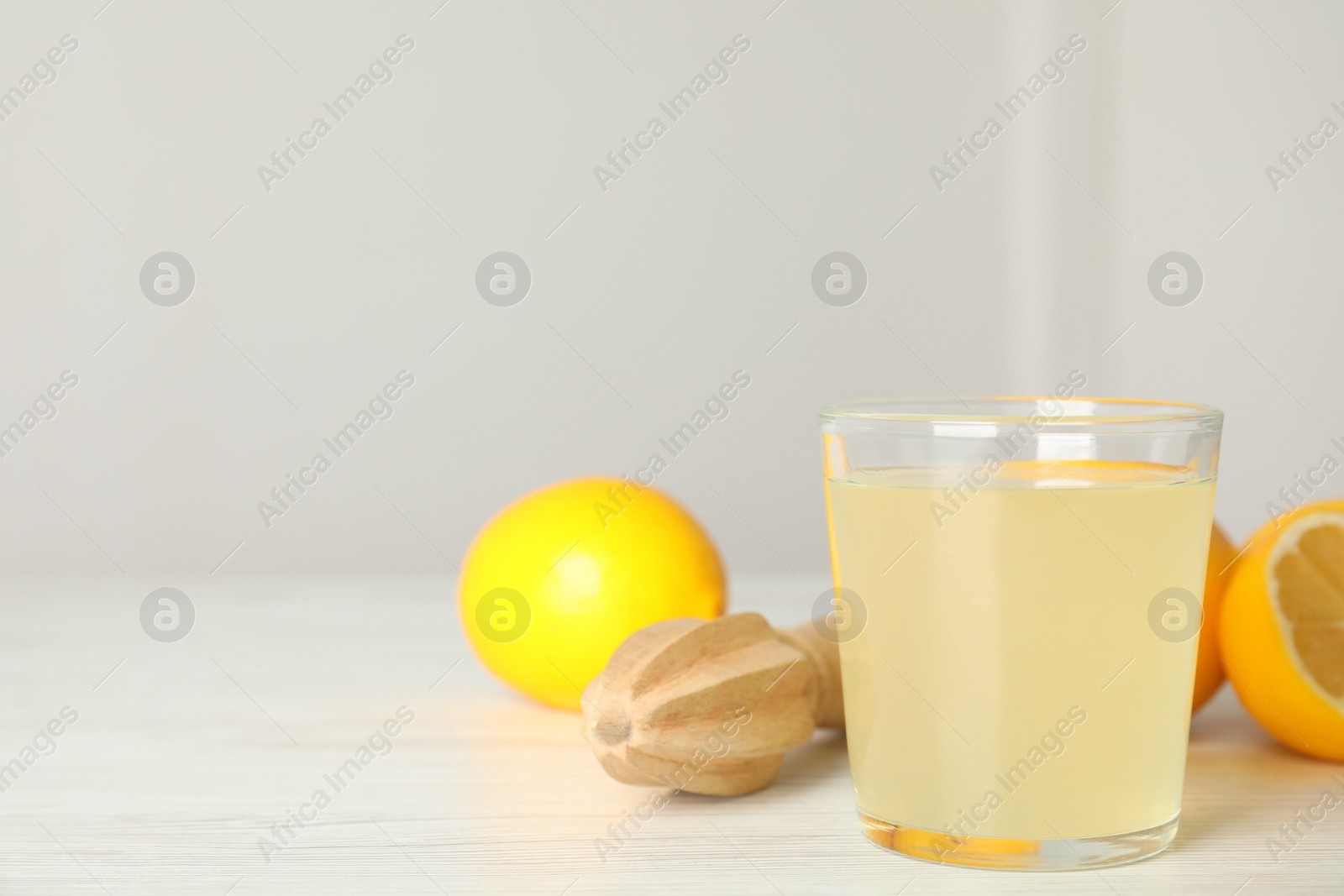 Photo of Freshly squeezed juice, lemons and reamer on white wooden table. Space for text