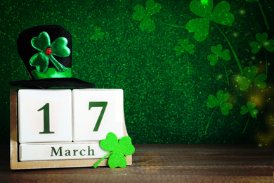 Black leprechaun hat, clover leaf and wooden block calendar on table, space for text. St. Patrick's Day celebration