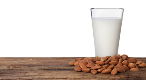 Almond milk in glass near nuts on wooden table against white background