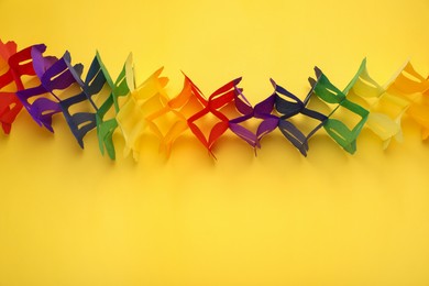 Photo of Rainbow paper garland on yellow background. LGBT pride