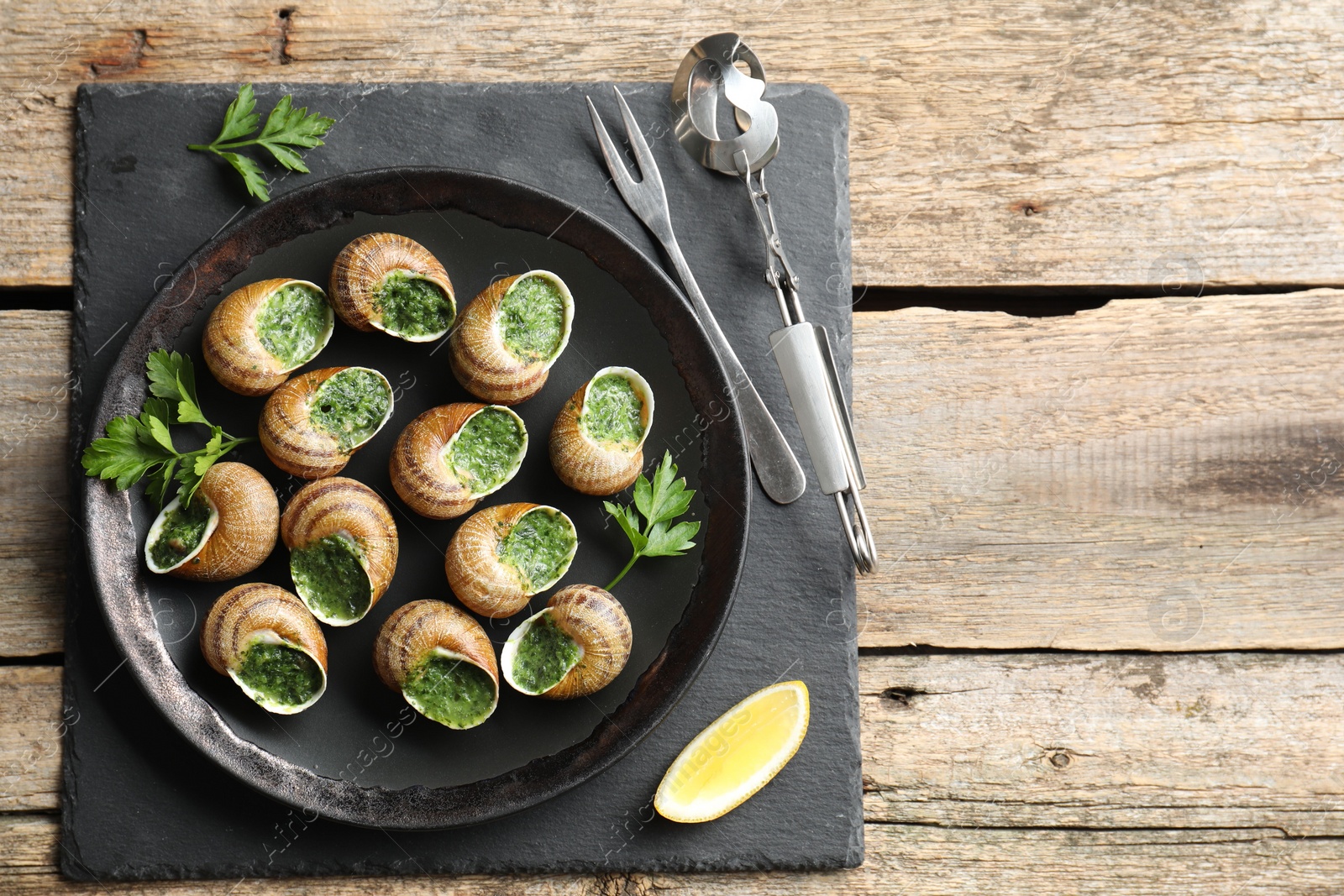 Photo of Delicious cooked snails served on wooden table, flat lay. Space for text