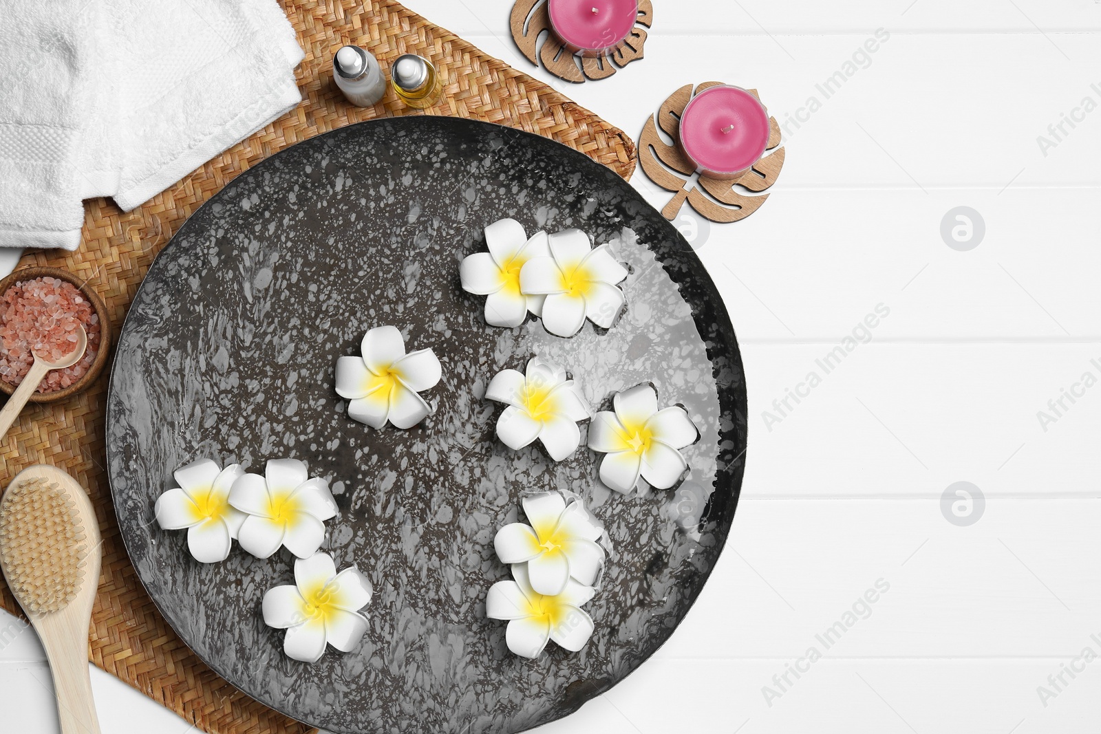 Photo of Bowl of water with flowers and different spa supplies on white wooden table, top view. Space for text