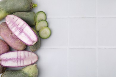 Photo of Purple and green daikon radishes on white tiled table, flat lay. Space for text