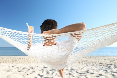 Man with refreshing cocktail relaxing in hammock on beach