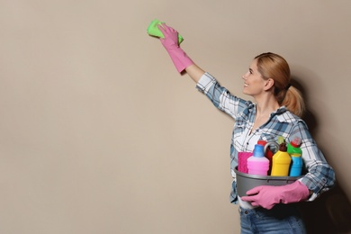 Woman with basin of detergents cleaning color wall. Space for text